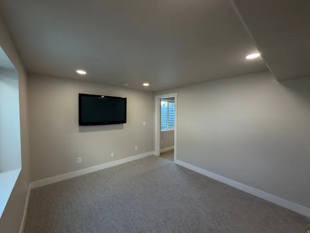 Recessed ceiling lighting illuminates the room with light neutral wall tones, light gray carpeting, and white trim