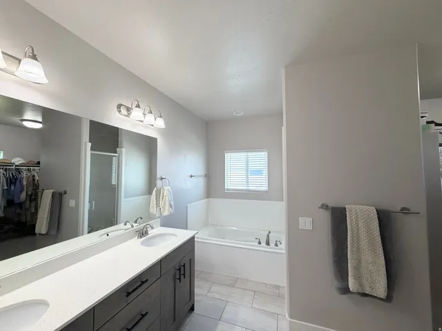 Dual vanity with undermount sinks and dark wood-finish cabinetry, a large built-in mirror, a built-in bathtub, and light-toned tile flooring