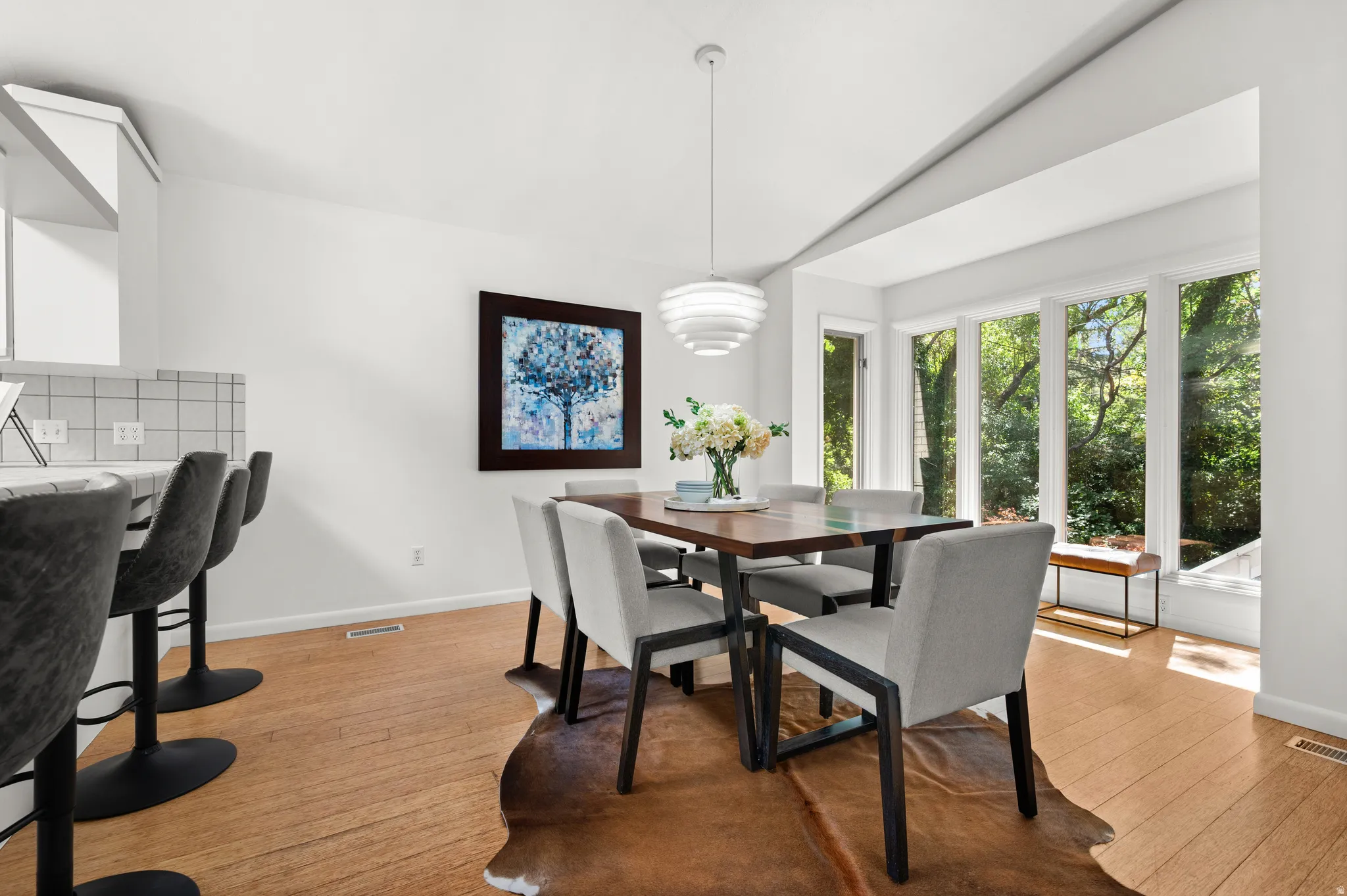 A wall of windows surrounds the dining area with mature trees and natural light.