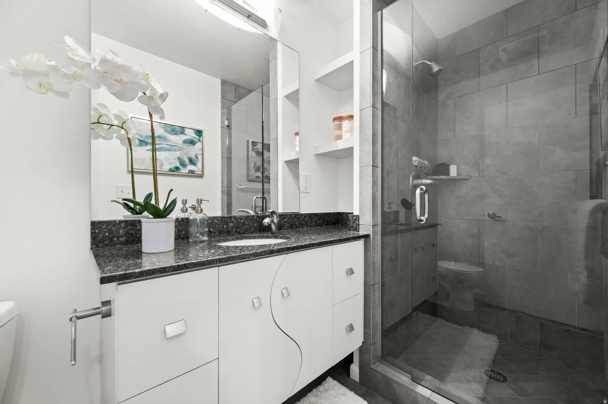 Updated main-level bath with granite countertop and a spacious glass-enclosed tiled shower.