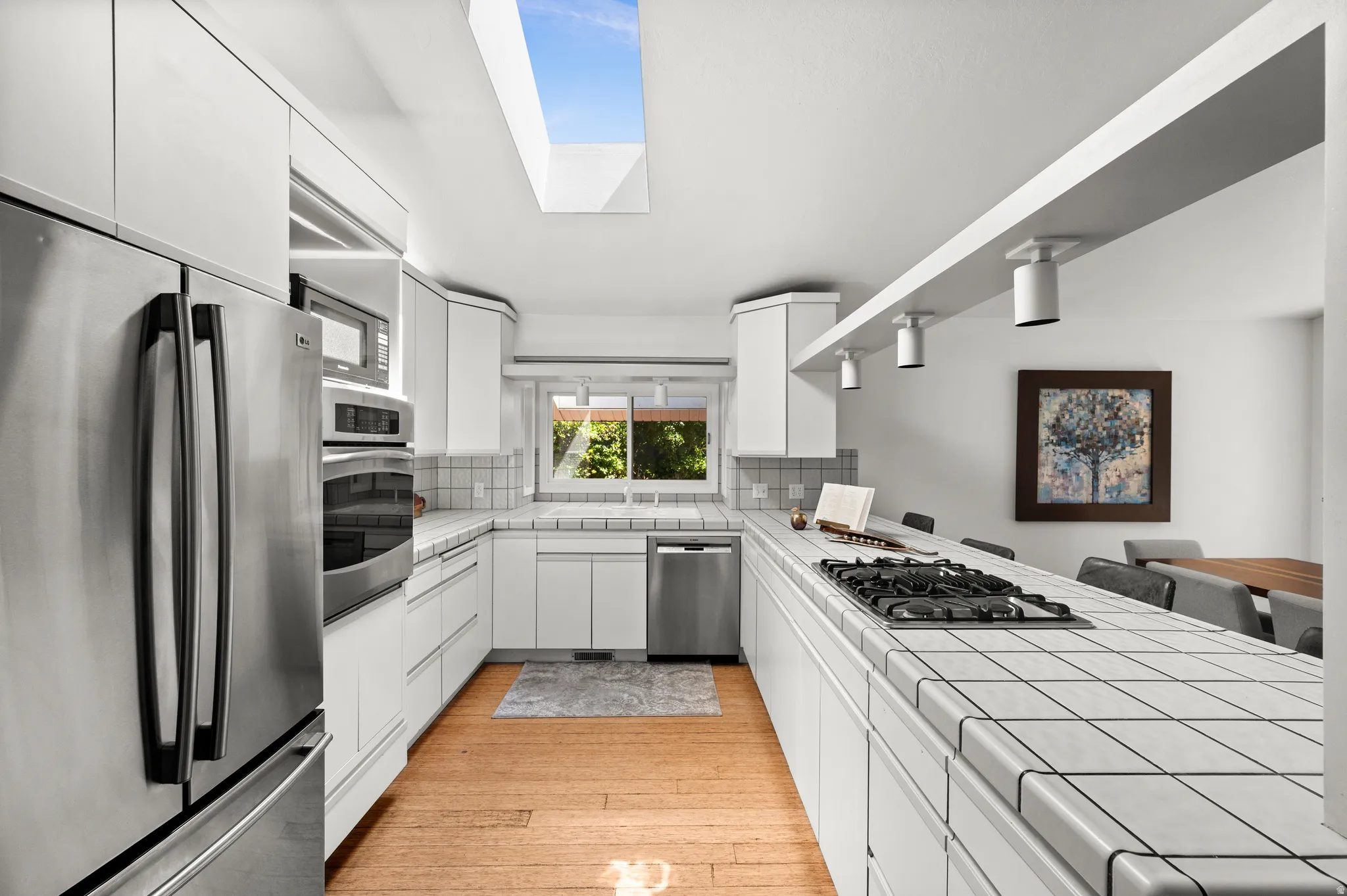 A spacious kitchen with abundant cabinetry, stainless appliances, skylight and a long peninsula opens to the dining area.