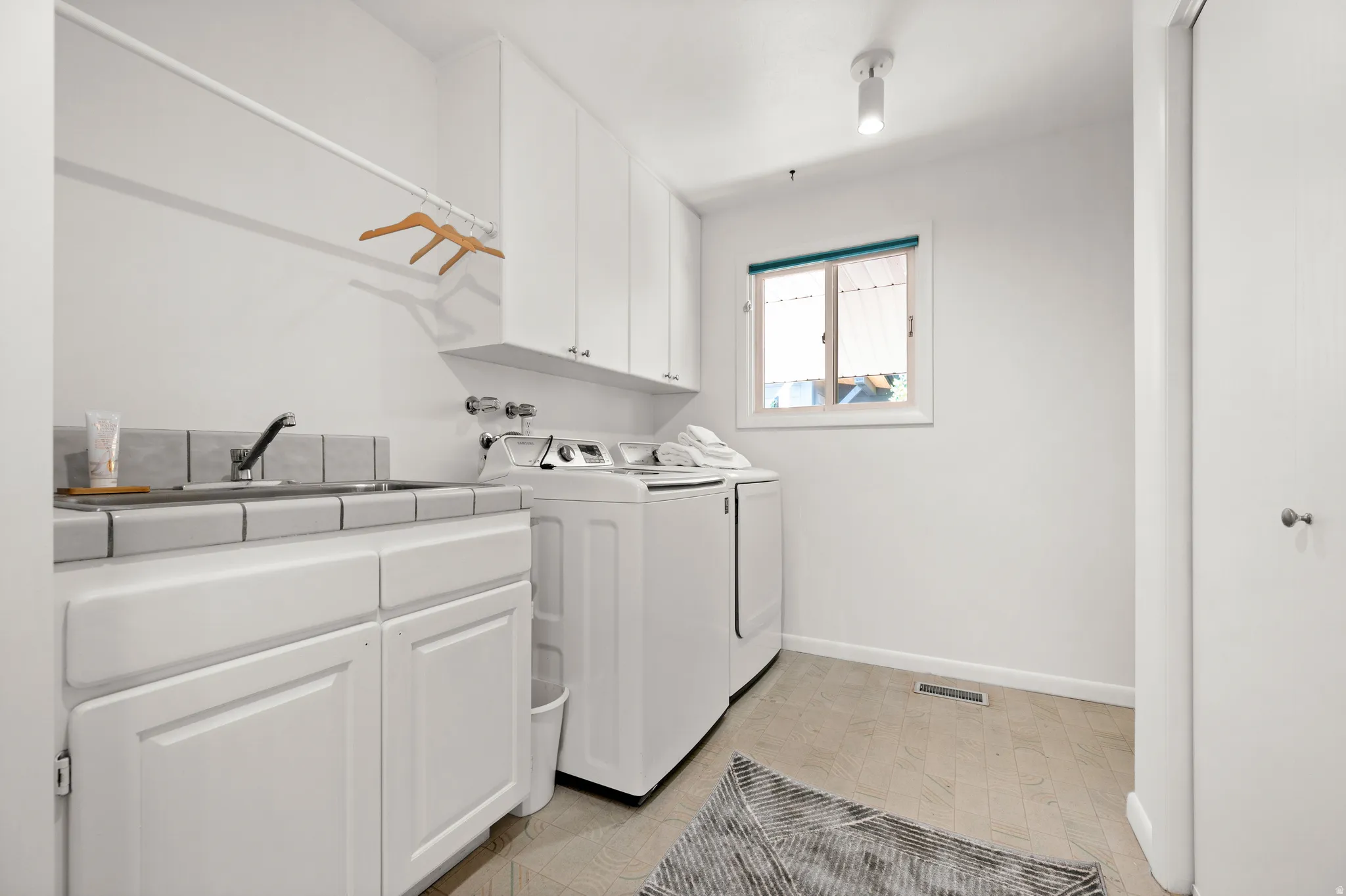 Main-level laundry with utility sink, cabinetry and additional storage.