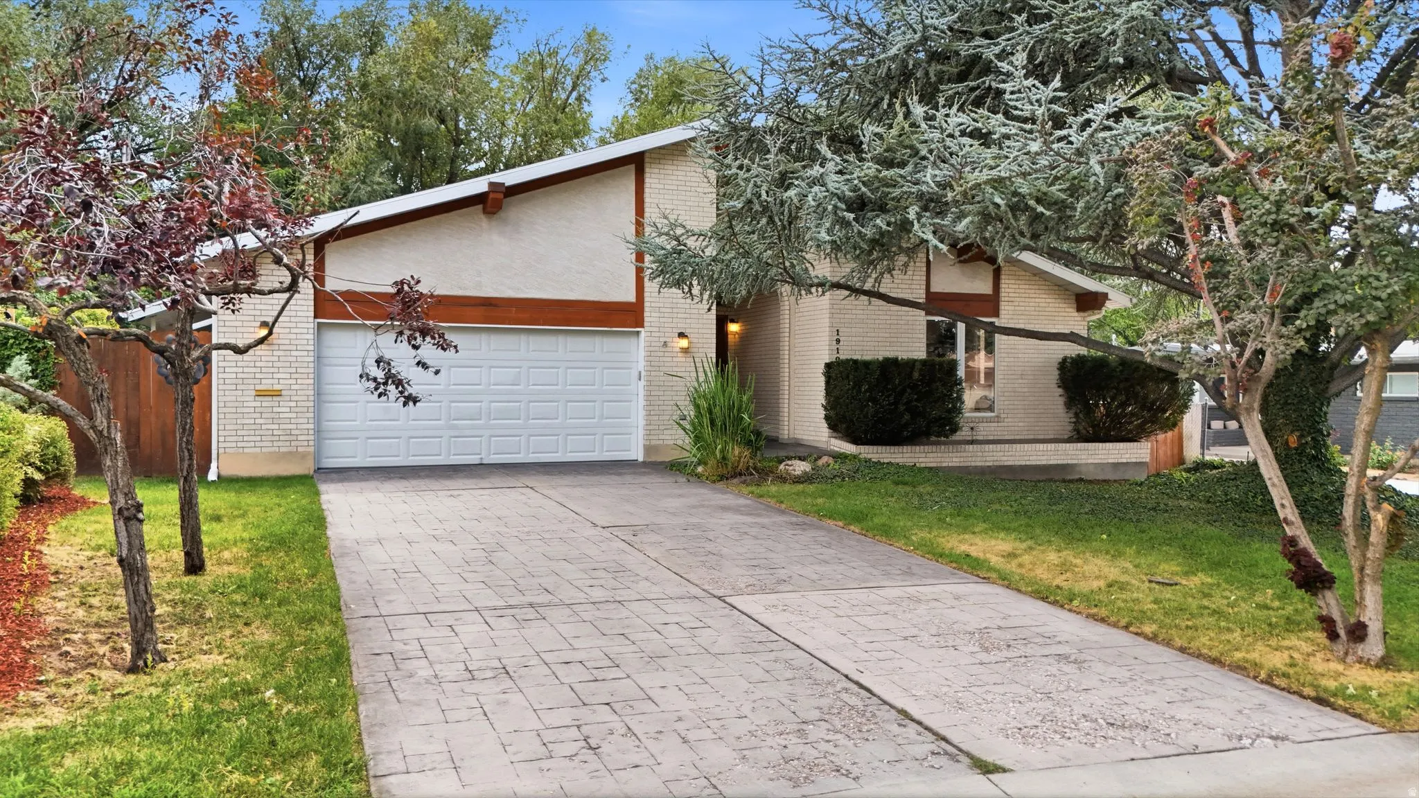 Stucco and brick exterior with a sloped roofline, attached garage, and stamped concrete driveway