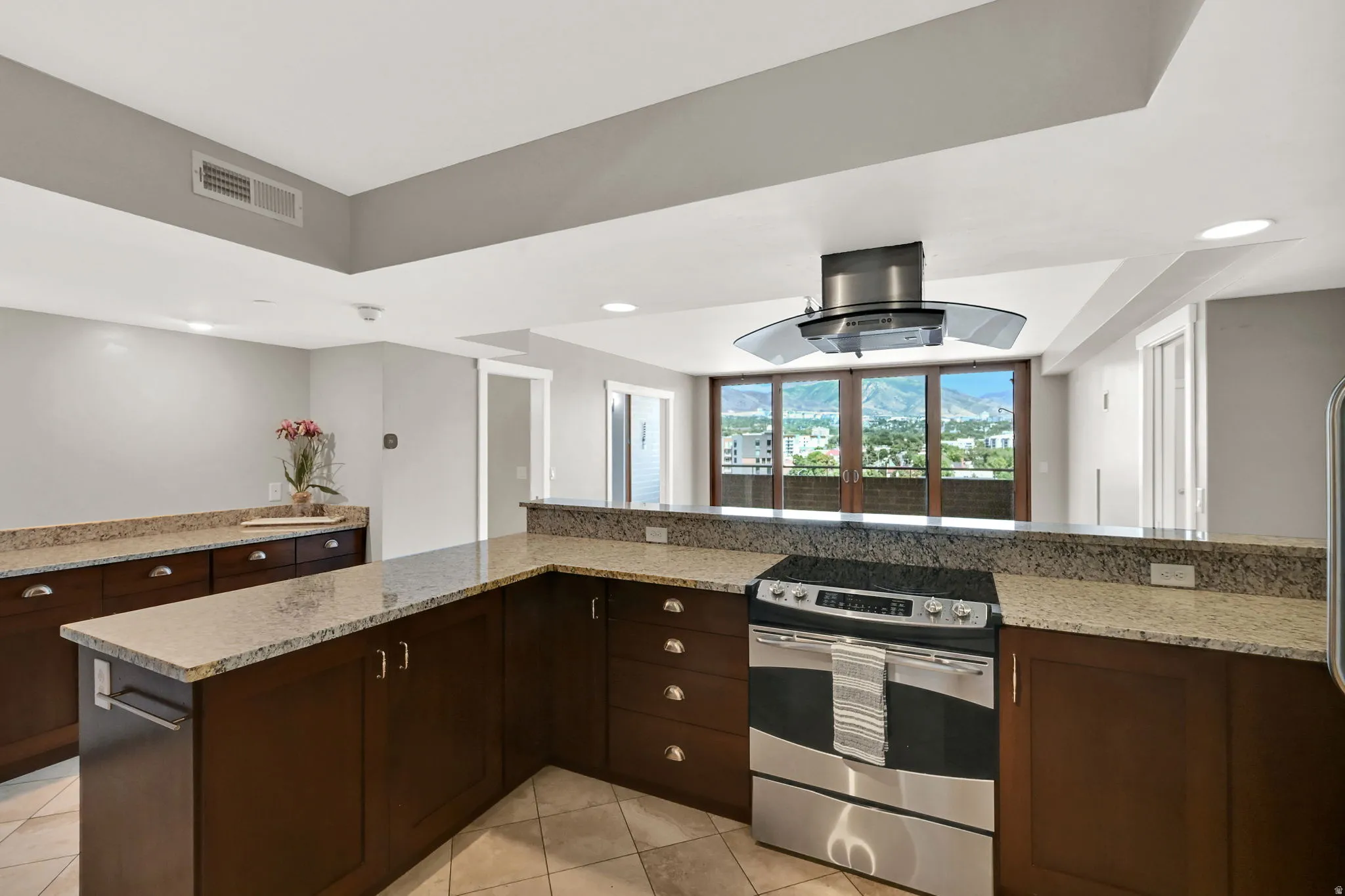 Kitchen featuring a stainless steel range, a coordinating range hood, granite countertops, dark wood-finish cabinetry, and tiled flooring