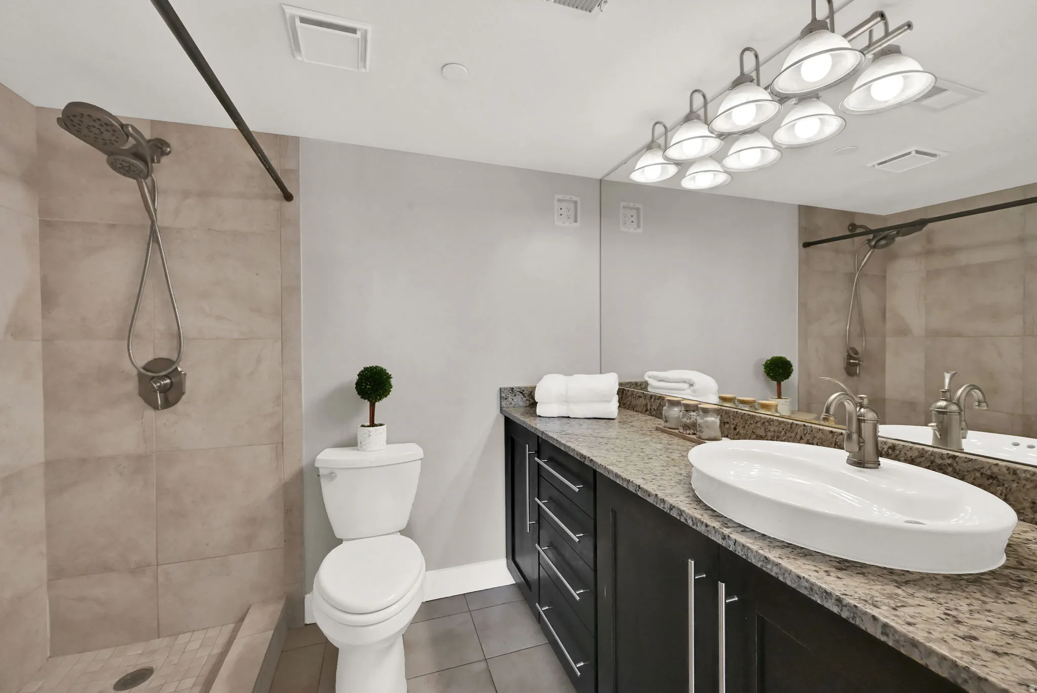 Primary bathroom.  Walk-in shower with tiled surround, vessel sink, vanity with ample storage, large mirror, and multi-bulb vanity lighting