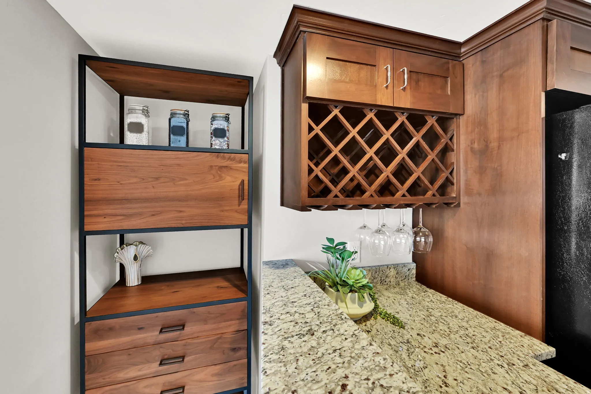 Built-in wood cabinetry with integrated wine rack, granite-finish countertop, and a contemporary wood and metal shelving unit