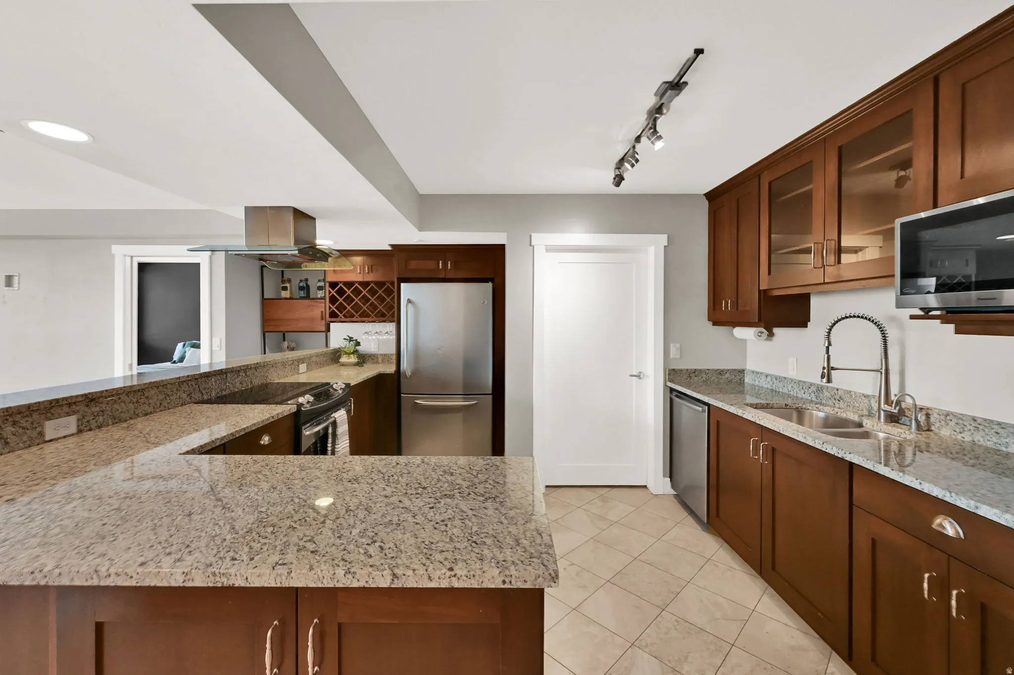 Open-concept kitchen featuring wood cabinetry, granite countertops, stainless steel appliances, undermount sink and tiled flooring