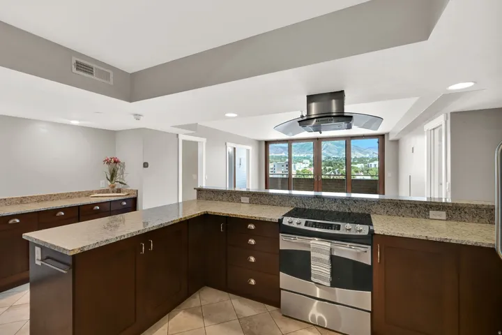 Kitchen featuring a stainless steel range, a coordinating range hood, granite countertops, dark wood-finish cabinetry, and tiled flooring