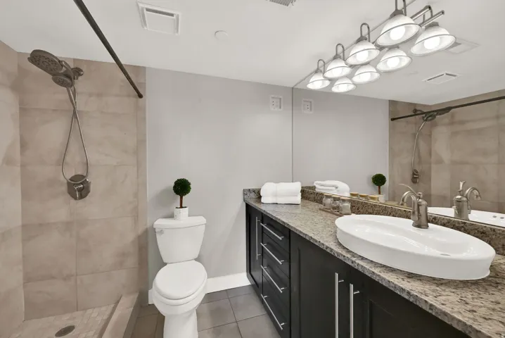 Primary bathroom.  Walk-in shower with tiled surround, vessel sink, vanity with ample storage, large mirror, and multi-bulb vanity lighting