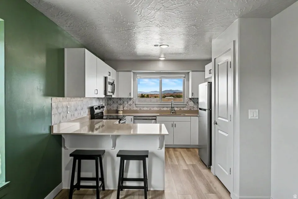 Kitchen featuring white cabinetry, wood-finish flooring, light-toned countertops, and a patterned tile backsplash
