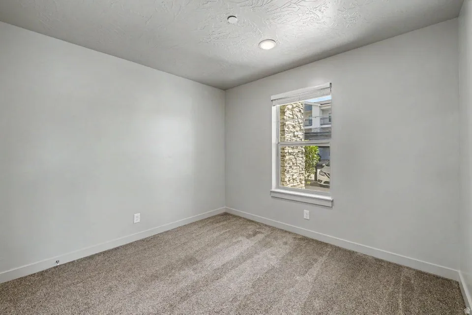 Neutral tone painted walls, textured ceiling, recessed lighting, carpet flooring, and a window with blinds
