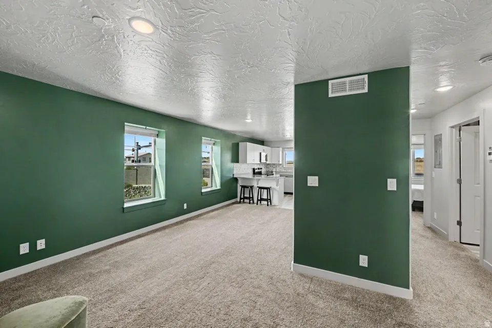 Open-concept living space with recessed lighting, carpeted flooring, and a kitchen featuring white cabinetry and a breakfast bar