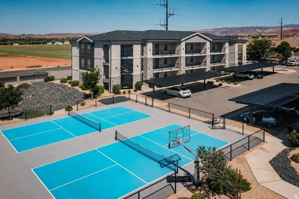 Multi-story building with stone and stucco exterior, covered parking structures, and multiple outdoor courts for recreation