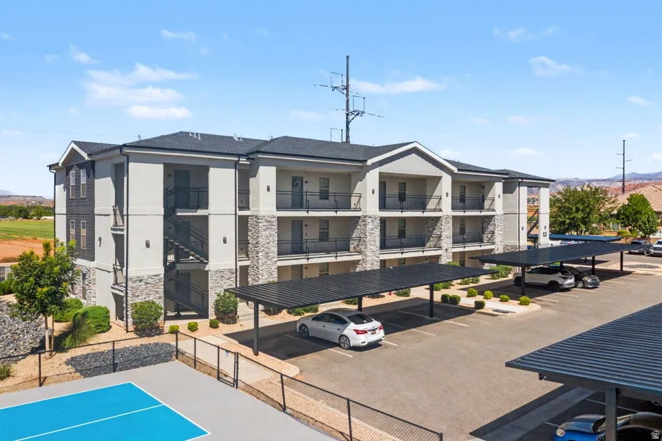 Multi-level building with stone and stucco exterior, covered parking structures, and balconies with black railings