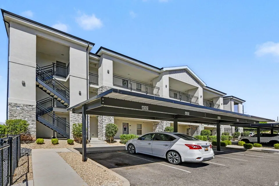 Multi-story building featuring exterior staircases with black railings, stone veneer accents, individual balconies, and covered parking