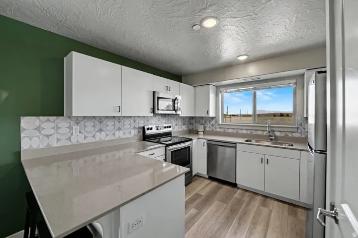 Kitchen featuring white cabinetry, light-toned countertops, a patterned tile backsplash, stainless steel appliances, and wood-finish flooring