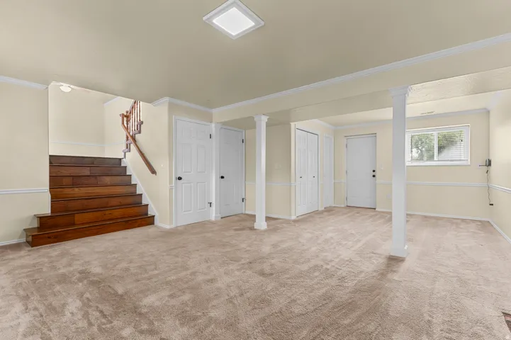 Spacious room with plush carpeting, wood stairs, a square ceiling light, and multiple storage doors