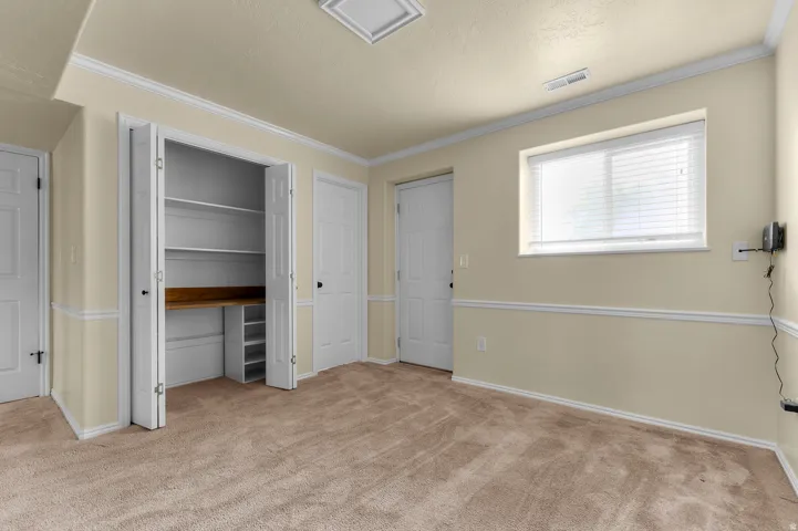 Wall-to-wall carpeting, window with blinds, recessed lighting, crown molding, and built-in desk with shelving