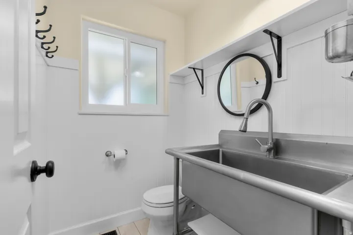 White shiplap wall paneling, stainless steel utility sink, frosted window, black matte hardware, and integrated shelving