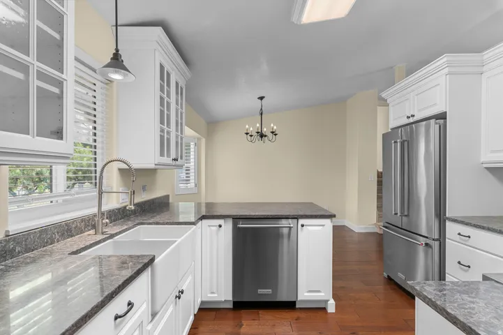White cabinetry with glass-front uppers, stainless steel appliances, dark stone-finish countertops, apron-front sink, and wood-finish flooring