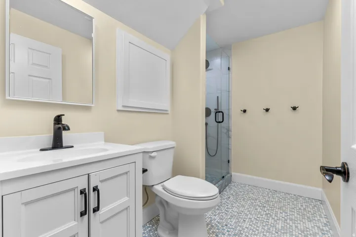 White vanity with solid surface countertop, matte black faucet, frameless mirror, and glass-enclosed shower with subway tile surround