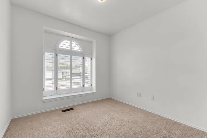 Arched window with plantation shutters, white trim, and neutral carpeting