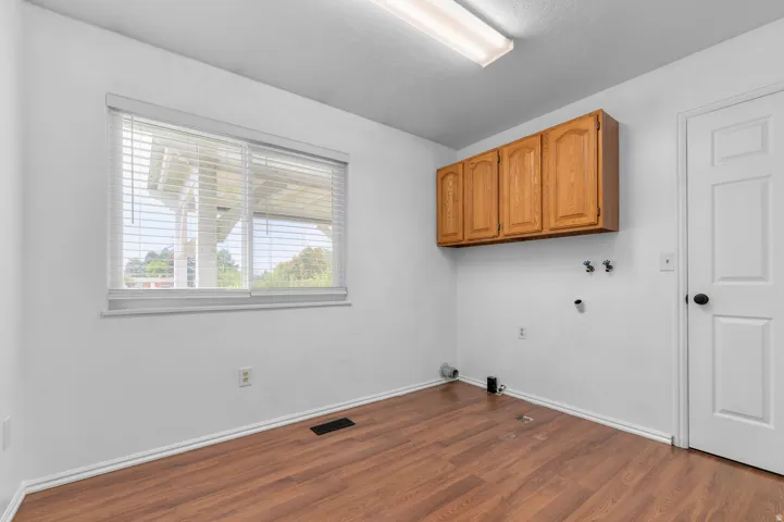 Wood-finish flooring, overhead lighting, window with blinds, wood cabinetry, and a white interior door