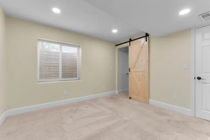 Recessed lighting, wood-finish barn door, window with blinds, light-colored carpeting, and white trim