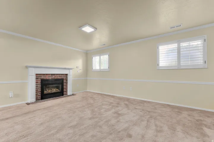 Brick fireplace with a white mantel, ceiling-mounted lighting, and two windows with white plantation shutters