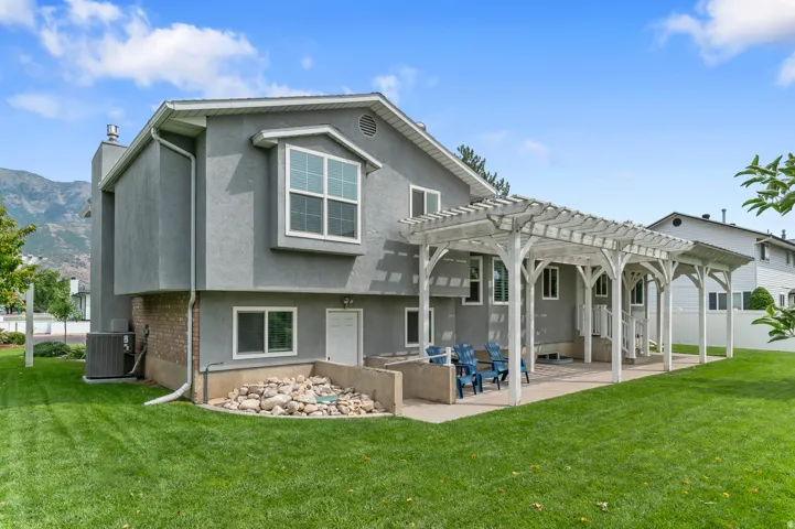 Expansive concrete patio with a white pergola structure, featuring a stucco exterior and a bay window