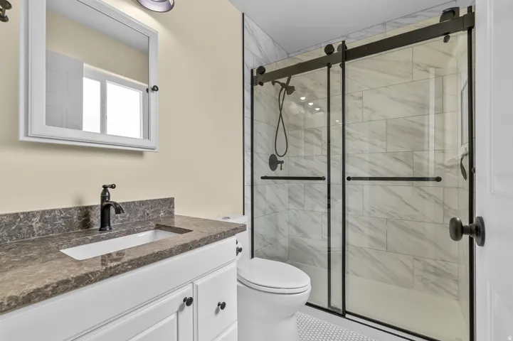 Bathroom featuring a single vanity with a stone countertop, a white rectangular sink, matte black faucet, and a shower with sliding glass doors and tiled walls