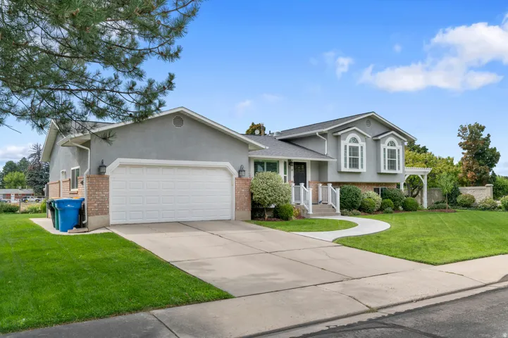 Stucco exterior with brick accents, attached two-car garage, white bay windows, concrete driveway, and a curving front walkway