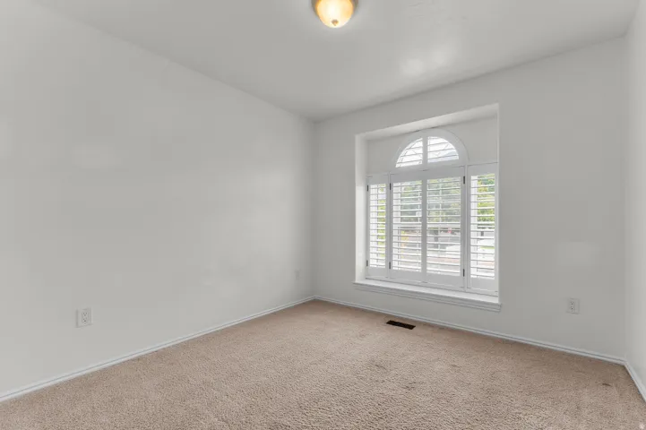 Arched window with plantation shutters, neutral wall color, and plush carpet flooring