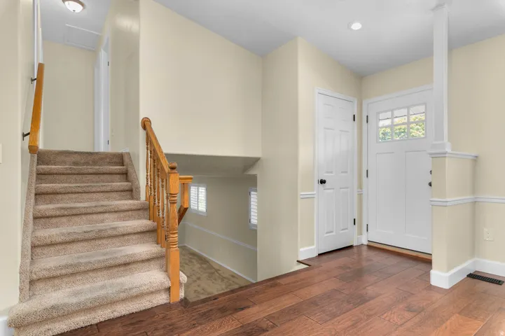 Wood-finish flooring, white paneled interior doors, a craftsman-style front door with glass panes, and a carpeted staircase with a wood banister