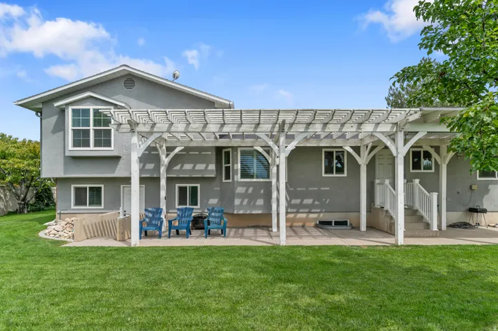Expansive lawn area with a concrete patio, white wood pergola, and exterior stairs with railing