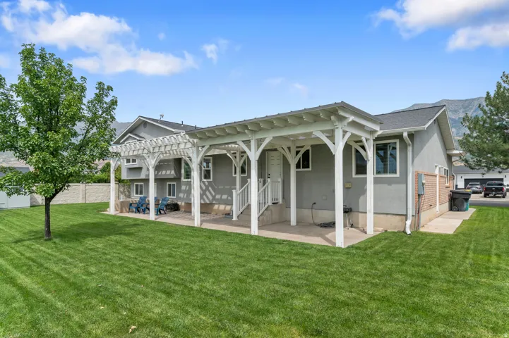 Expansive green lawn, white wood pergola, concrete patio space, and stucco exterior