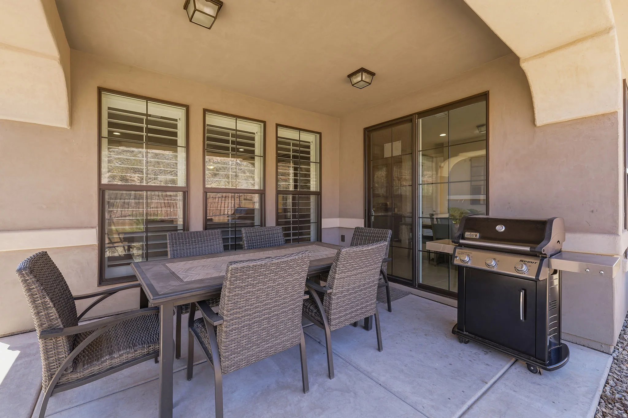Covered patio featuring concrete flooring and stucco walls, with multiple windows and a sliding glass door