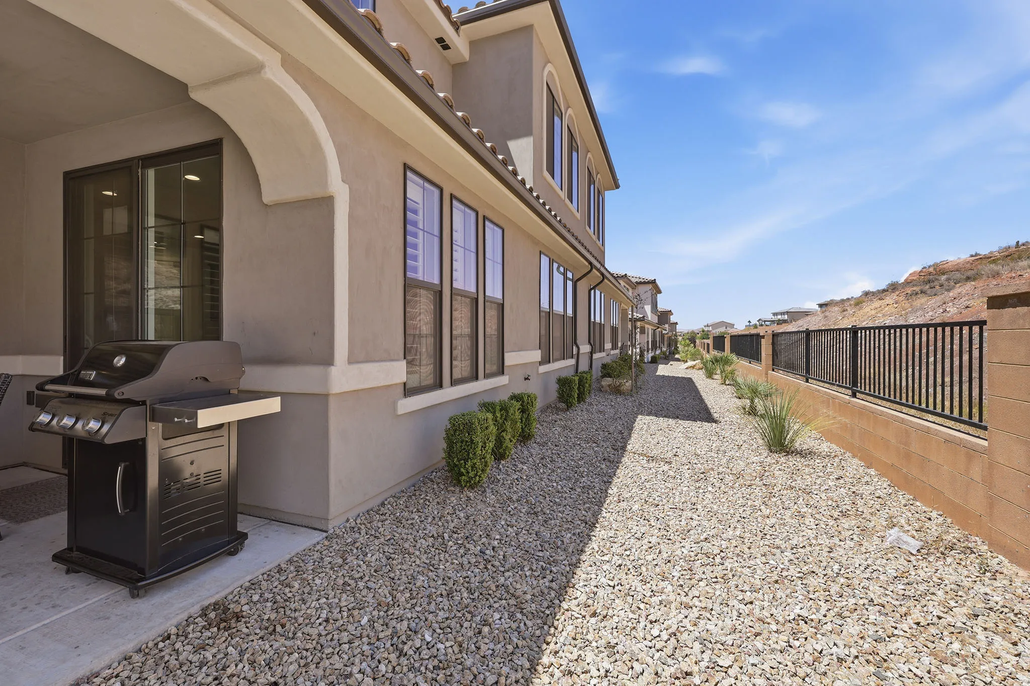 Stucco exterior with multiple windows, covered patio, gravel landscaping, and a block wall with metal fencing