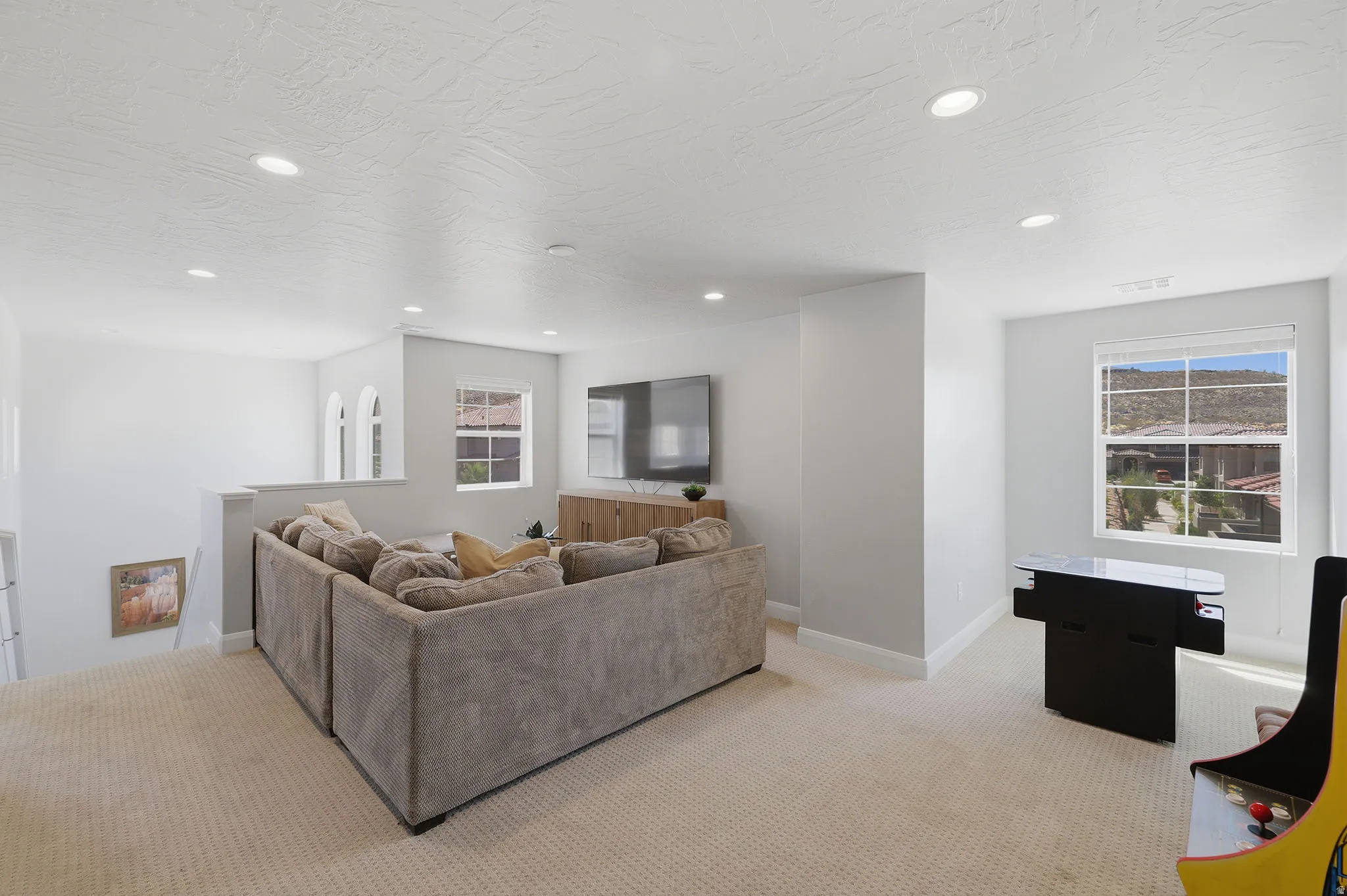 Carpeted loft space with recessed lighting, multiple windows, and a built-in wood-finish media console