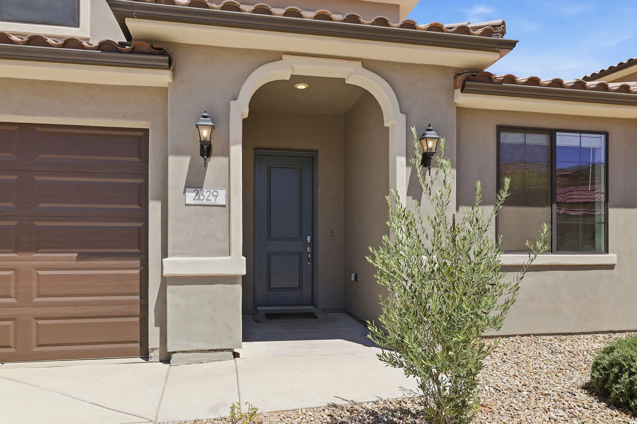 Arched entryway with a paneled door, exterior sconce lighting, and an attached garage with a wood-finish door