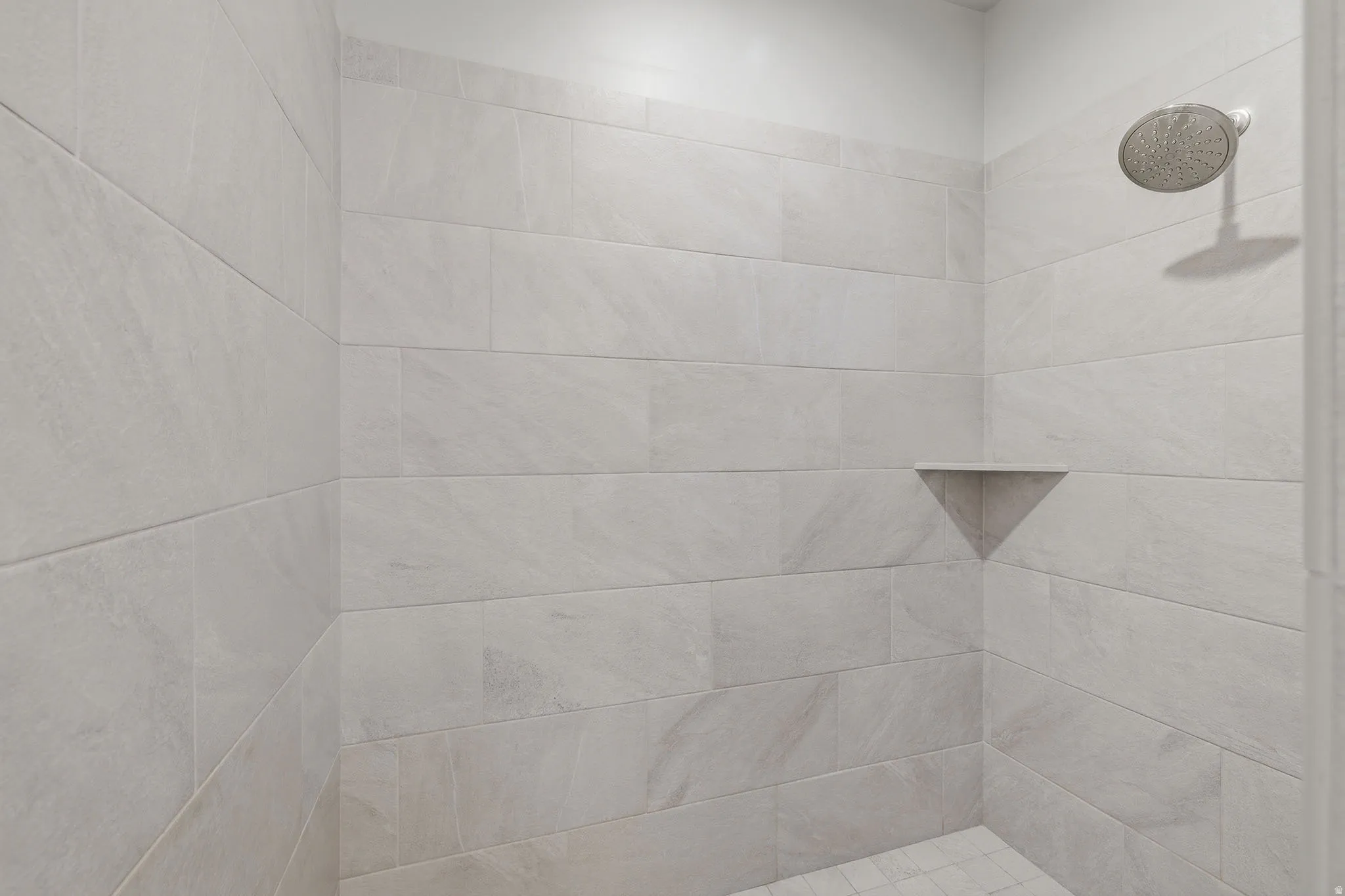 Shower stall with light-toned rectangular wall tiling, integrated corner shelf, and a ceiling-mounted shower head