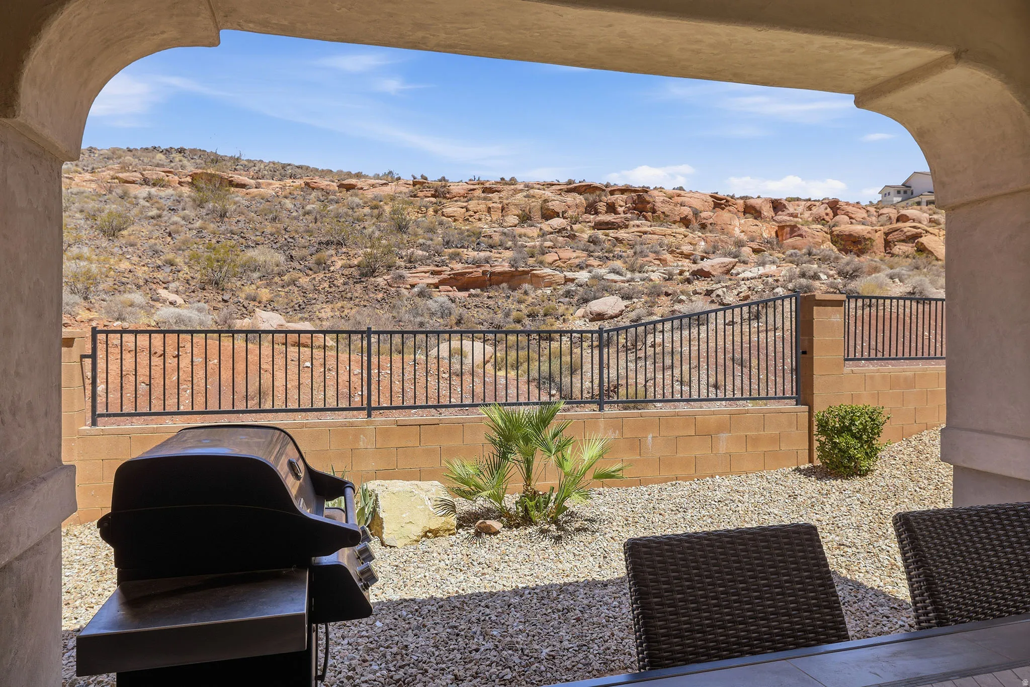 Covered patio with an arched opening, desert rock landscaping, low-maintenance gravel, and wrought iron fencing