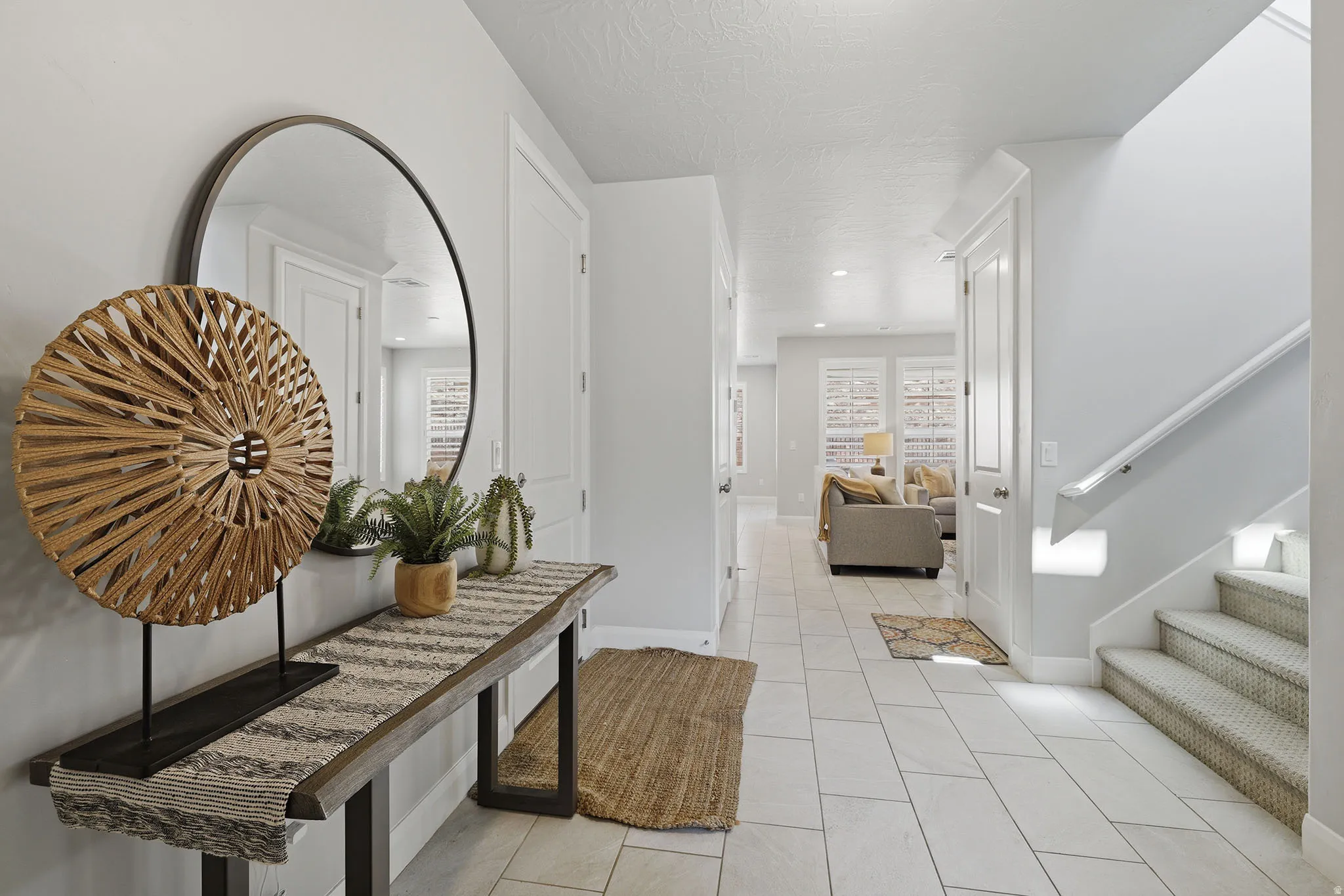 Tiled entryway with a round wall mirror, console table, and staircase with carpeted treads