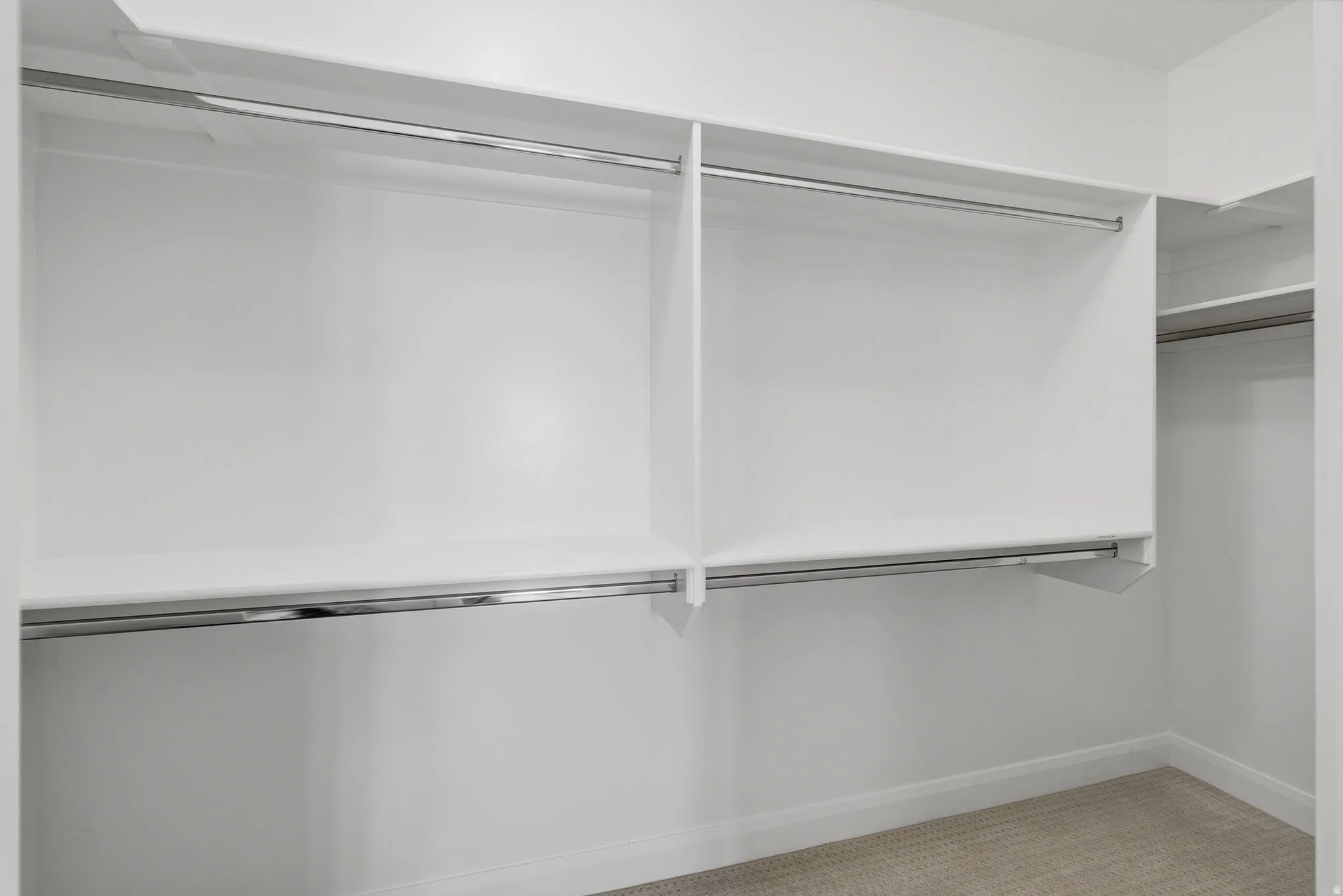 White built-in closet shelving, chrome hanging rods, and light-colored carpet flooring