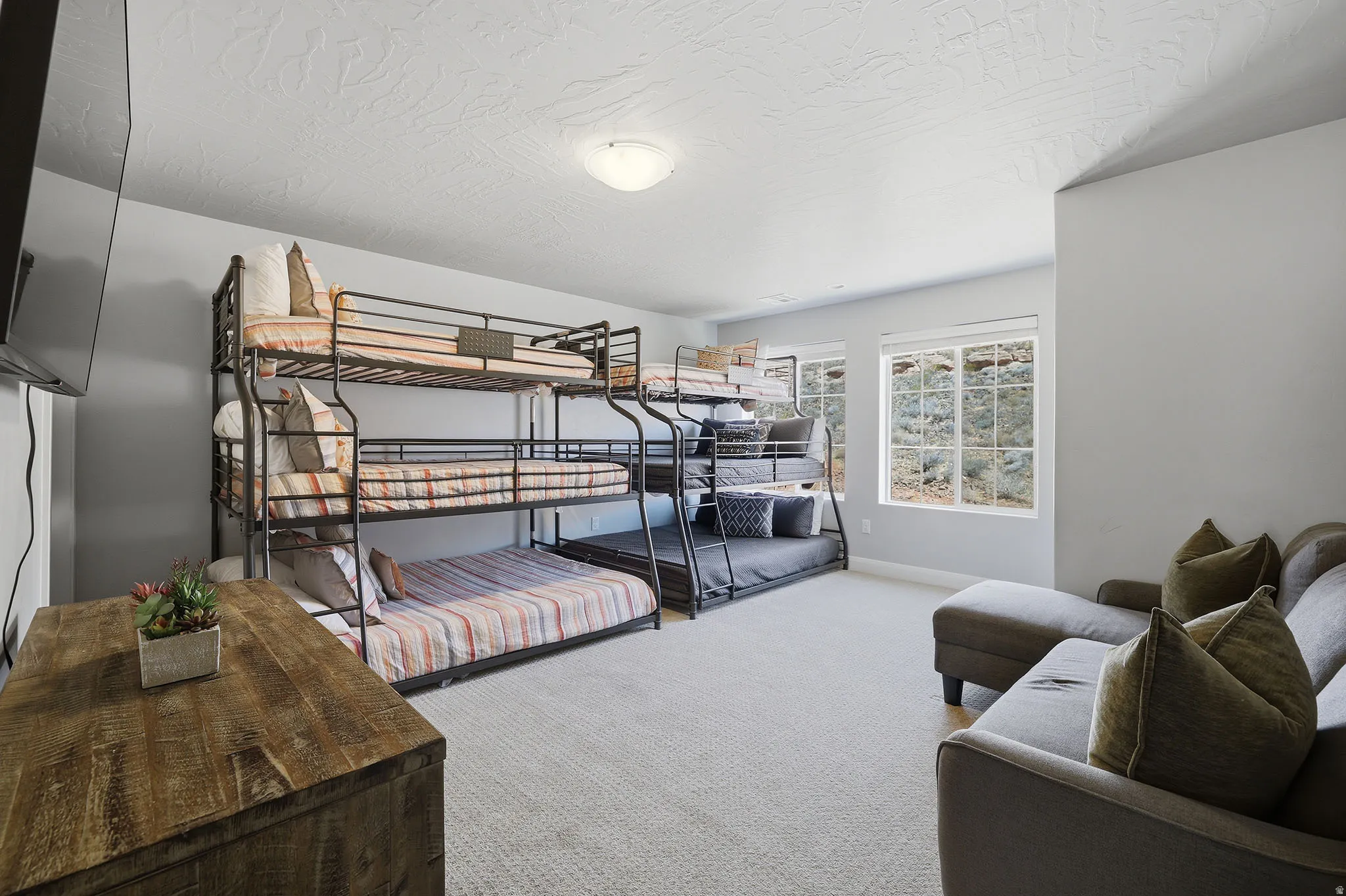 Carpeted room featuring dual multi-level bunk beds, a rustic wood-finish dresser, and multiple windows