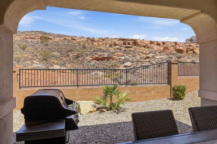 Covered patio with an arched opening, desert rock landscaping, low-maintenance gravel, and wrought iron fencing