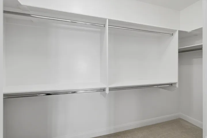 White built-in closet shelving, chrome hanging rods, and light-colored carpet flooring