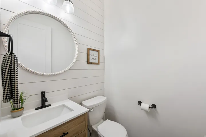 Bathroom featuring shiplap accent wall, wood-finish vanity, white countertop with integrated sink, and black matte faucet