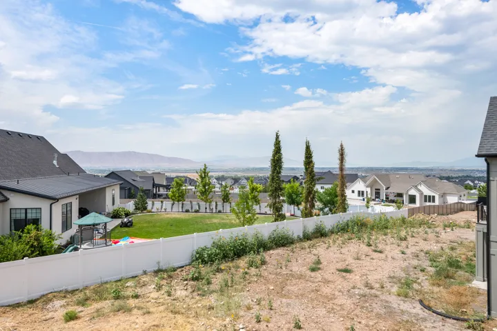 Expansive backyard featuring a manicured lawn, established trees, and a white privacy fence