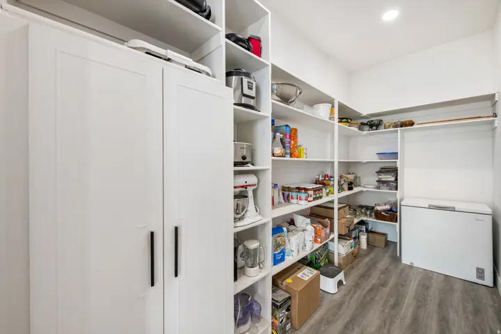 Expansive pantry featuring extensive shelving, white cabinetry with matte black hardware, and wood-finish flooring
